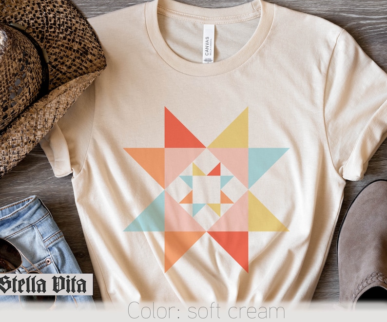 May include: A soft cream t-shirt with a colorful geometric star design. The star is made up of triangles in shades of pink, orange, yellow, and blue. The shirt is a simple, casual style with a crew neck and short sleeves. "Stella Vita" is written in black at the bottom left of the image. "Color: soft cream" is written in black at the bottom right of the image.