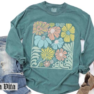 Peut inclure: Chemise &agrave; manches longues turquoise avec un imprim&eacute; floral color&eacute;. L'imprim&eacute; pr&eacute;sente une vari&eacute;t&eacute; de fleurs dans des tons de rose, jaune et vert.