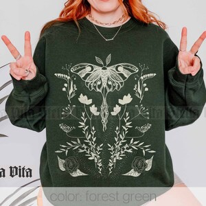 May include: Forest green sweatshirt with a white graphic of a moth and floral design. The text "Stella Vita" is visible in the bottom left corner of the image.