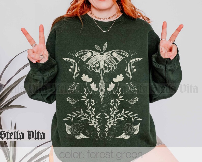 May include: Forest green sweatshirt with a white graphic of a moth and floral design. The text "Stella Vita" is visible in the bottom left corner of the image.