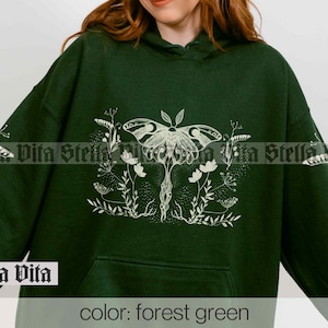 May include: Forest green hooded sweatshirt with a white graphic print of a moth and floral design. The text "Stella Vita" is printed on the bottom left corner of the sweatshirt.