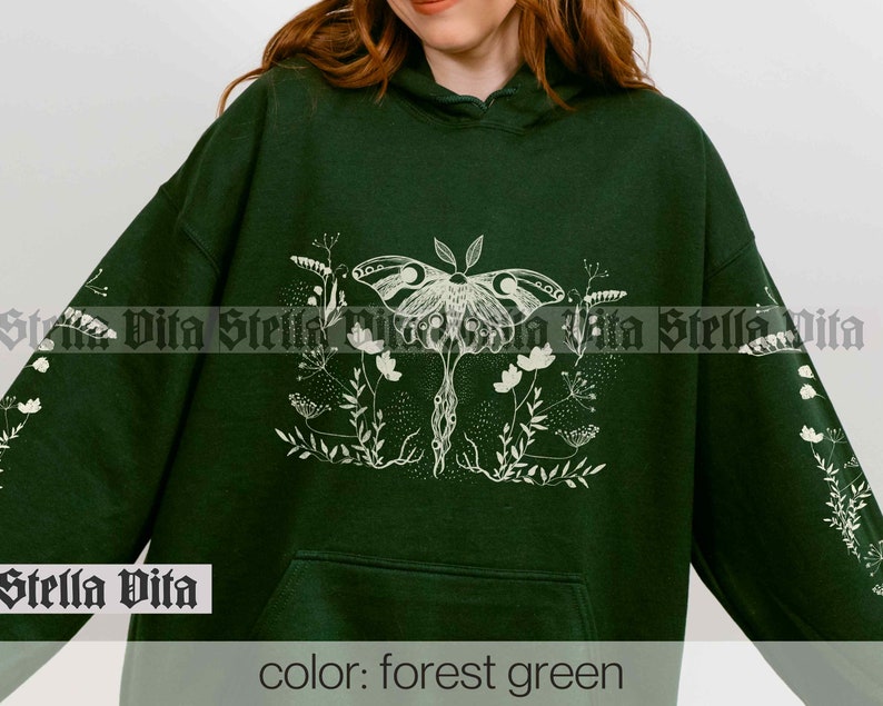 May include: Forest green hooded sweatshirt with a white graphic print of a moth and floral design. The text "Stella Vita" is printed on the bottom left corner of the sweatshirt.