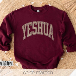 May include: Maroon sweatshirt with the word "YESHUA" in gold lettering on the front.
