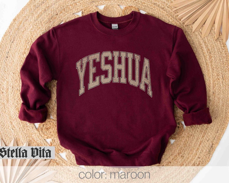May include: Maroon sweatshirt with the word "YESHUA" in gold lettering on the front.