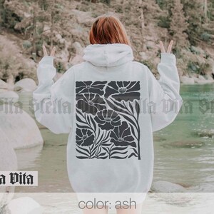 May include: A white hoodie with a black floral design. The hoodie has a drawstring hood and a kangaroo pocket. The text "color: ash" is printed on the bottom of the hoodie.