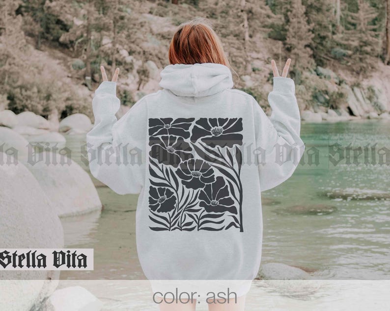 May include: A white hoodie with a black floral design. The hoodie has a drawstring hood and a kangaroo pocket. The text "color: ash" is printed on the bottom of the hoodie.