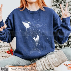 May include: A navy blue sweatshirt with a white graphic of an orca whale swimming through a starry sky. The text "North Pole" is visible on a white surface in the background.