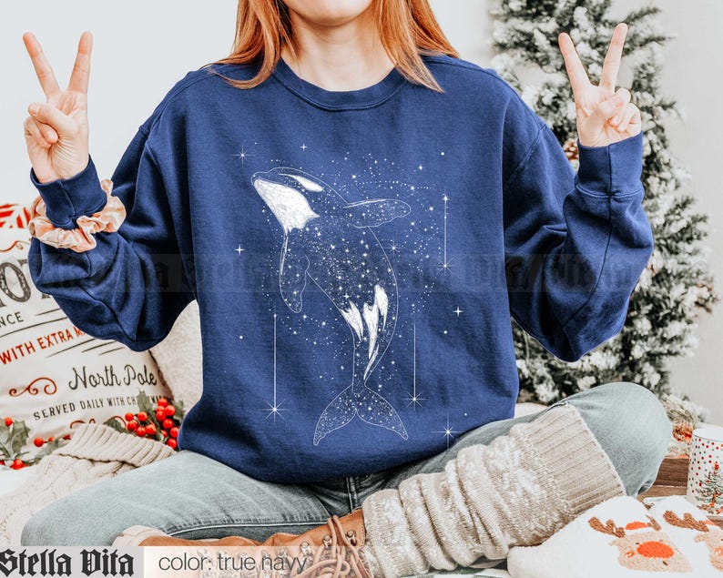 May include: A navy blue sweatshirt with a white graphic of an orca whale swimming through a starry sky. The text "North Pole" is visible on a white surface in the background.