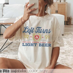 May include: Ivory-colored t-shirt with the text "Left Turns" in blue and yellow. The shirt also features the text "BURNING RUBBER SINCE 1985 LIGHT BEER". The shirt is part of the "comfort colors" collection.