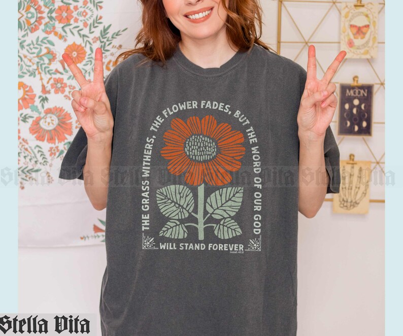 May include: A dark gray t-shirt with a graphic of a sunflower and the text "The grass withers, the flower fades, but the word of our God will stand forever."