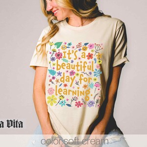May include: A cream coloured t-shirt with a floral design and the text "It's a beautiful day for learning."