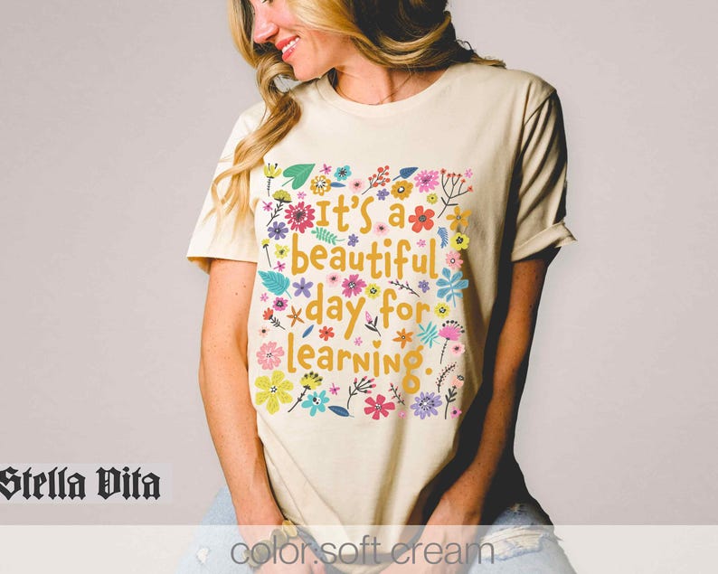 May include: A cream coloured t-shirt with a floral design and the text "It's a beautiful day for learning."
