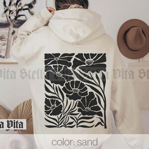 May include: A sand-colored hoodie with a black floral design on the back. The design features stylized flowers with black stems and leaves.