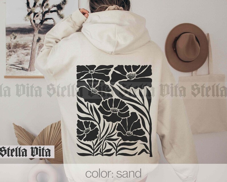 May include: A sand-colored hoodie with a black floral design on the back. The design features stylized flowers with black stems and leaves.