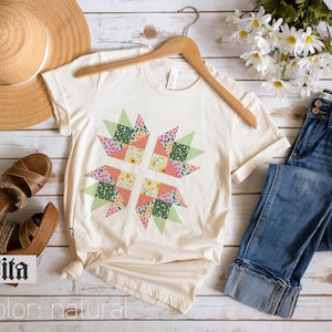 May include: A natural colored t-shirt with a colorful patchwork design in the shape of a star. The shirt is on a wooden surface with a pair of brown sandals, a straw hat, and a pair of blue jeans.