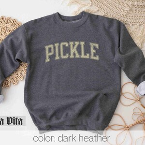May include: A dark heather grey sweatshirt with the word "PICKLE" printed in a vintage-style font in a light yellow color.