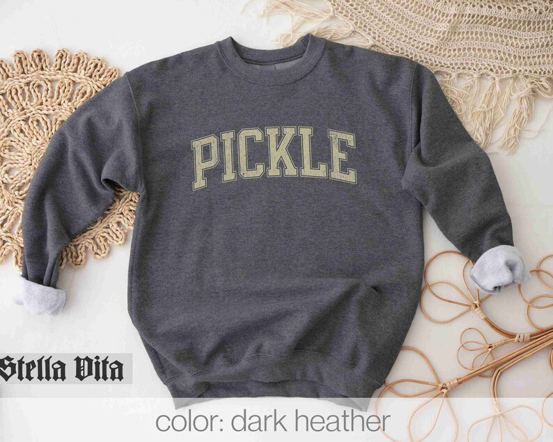 May include: A dark heather grey sweatshirt with the word "PICKLE" printed in a vintage-style font in a light yellow color.