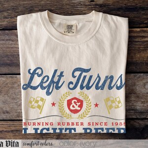 May include: Ivory-colored t-shirt with the text "Left Turns" in blue script. Below the text is a graphic with a shield, laurel wreath, and checkered flags. The shirt also has the text "BURNING RUBBER SINCE 1985 LIGHT BEER".