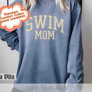 Puede incluir: Sudadera azul vaquero con el texto "SWIM MOM" en una fuente de estilo universitario vintage.