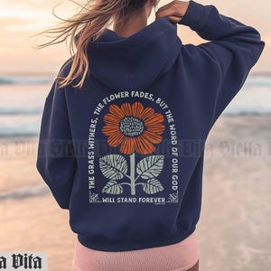 May include: Navy blue hooded sweatshirt with a graphic print of a sunflower and the text "THE GRASS WITHERS, THE FLOWER FADES, BUT THE WORD OF OUR GOD WILL STAND FOREVER."