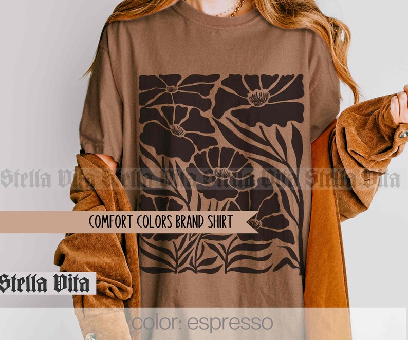 Puede incluir: Una camiseta marr&oacute;n con un dise&ntilde;o floral en negro. El dise&ntilde;o presenta flores estilizadas con p&eacute;talos grandes y hojas. El texto "COMFORT COLORS BRAND SHIRT" est&aacute; impreso en la camiseta. El color de la camiseta se describe como "espresso".