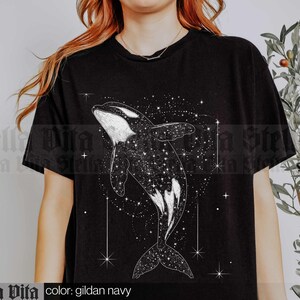 May include: A black t-shirt featuring a white graphic of an orca whale swimming through a starry sky. The text "color: gildan navy" is printed below the graphic.