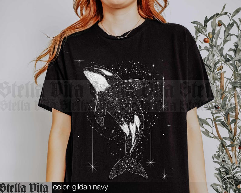 May include: A black t-shirt featuring a white graphic of an orca whale swimming through a starry sky. The text "color: gildan navy" is printed below the graphic.