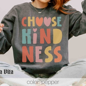 K&ouml;nnte beinhalten: Ein anthrazitfarbener Sweatshirt mit den Worten "Choose Kindness" in bunten Blockbuchstaben. Die Buchstaben sind wei&szlig; umrandet und haben eine Herzform in der Mitte des Wortes "Kindness".