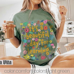 May include: A light green t-shirt with a floral design and the text "It's a beautiful day for learning."