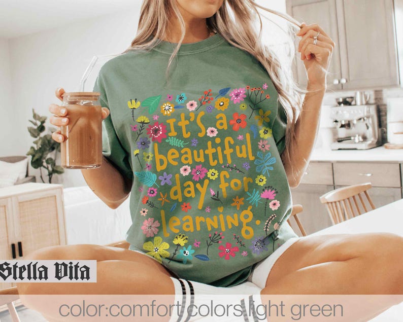 May include: A light green t-shirt with a floral design and the text "It's a beautiful day for learning."