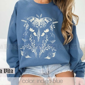 May include: Indigo blue sweatshirt with a white graphic of a moth and flowers. The text "Stella Vita" is visible at the bottom of the image.