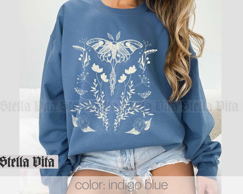 May include: Indigo blue sweatshirt with a white graphic of a moth and flowers. The text "Stella Vita" is visible at the bottom of the image.