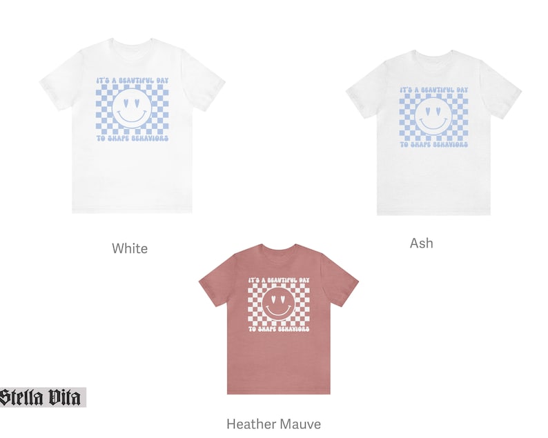 May include: Three t-shirts in different colors: white, ash, and heather mauve. Each shirt features a blue and white checkered pattern with a smiley face and the text "It's a beautiful day to shape behaviors".