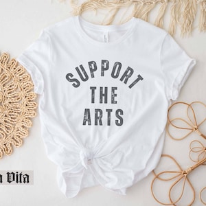May include: White t-shirt with the text "Support the Arts" printed in gray on the front.