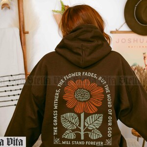 May include: Brown hooded sweatshirt with a graphic print of a sunflower and the text "The grass withers, the flower fades, but the word of our God will stand forever."