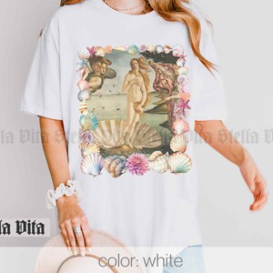 Puede incluir: Camiseta blanca con un gr&aacute;fico de la pintura El nacimiento de Venus rodeado de conchas.