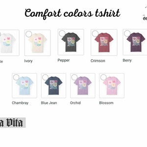 May include: A graphic t-shirt featuring a floral design in shades of pink, yellow, blue, and green. The shirt is available in ten different colours: white, ivory, pepper, crimson, berry, chambray, blue jean, orchid, and blossom.