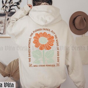 May include: A cream-colored hoodie with a floral graphic and the text "The grass withers, the flower fades, but the word of our God will stand forever."