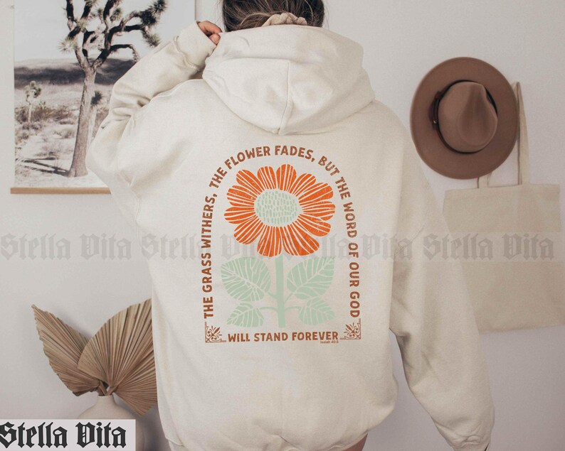 May include: A cream-colored hoodie with a floral graphic and the text "The grass withers, the flower fades, but the word of our God will stand forever."