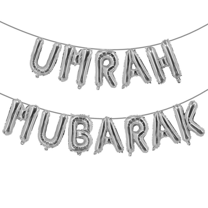 May include: Silver foil balloon letters spelling "UMRAH MUBARAK" strung together on a white background.
