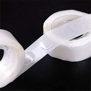 May include: Two rolls of clear adhesive tape with small, round, clear adhesive dots. The tape is white and the dots are clear. The tape is rolled up and the dots are visible on the outside of the roll.