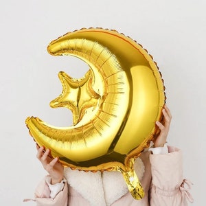 May include: A gold foil balloon shaped like a crescent moon with a star. The balloon is inflated and ready to be used for a party or celebration.