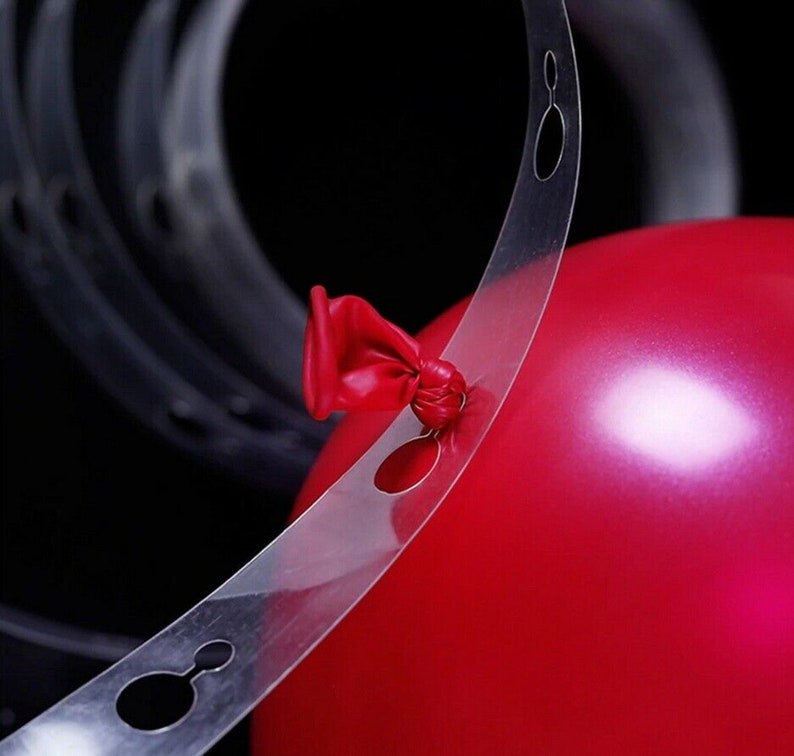 May include: A clear plastic balloon arch strip with holes for tying balloons. The strip is curved and has a red balloon tied to it.