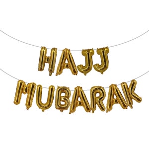 May include: Gold foil balloon letters spelling "HAJJ MUBARAK" hanging on a string.