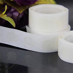 May include: A roll of white adhesive dots for attaching decorations to walls or other surfaces. The dots are clear and come in a roll with a dispenser.