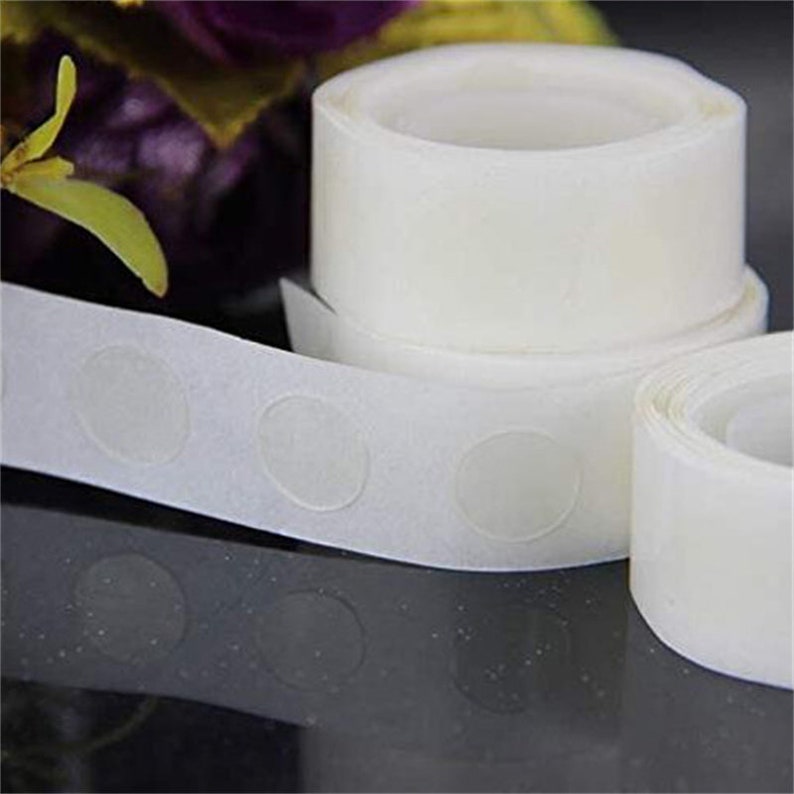 May include: A roll of white adhesive dots for attaching decorations to walls or other surfaces. The dots are clear and come in a roll with a dispenser.