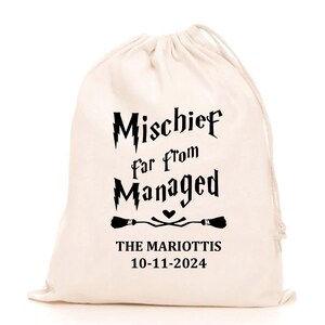 Könnte beinhalten: Cremefarbener Kordelzugbeutel mit schwarzem Text: "Mischief far from Managed". Darunter zwei Besen-Illustrationen und ein Herz. Der Text "THE MARIOTTI'S 10-11-2024" ist unter den Besen aufgedruckt.