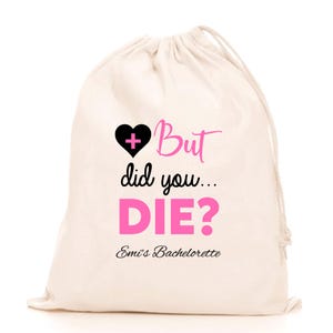 May include: A white cotton drawstring bag with a pink heart with a black plus sign and the text "But did you... DIE?" in pink. The text "Emi's Bachelorette" is printed below in black.