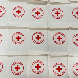 May include: A collection of off-white rectangular fabric pouches arranged in a grid. Each pouch features a red circular emblem containing a red cross and the text "IN SICKNESS & IN HEALTH" printed in a circular pattern around the cross.