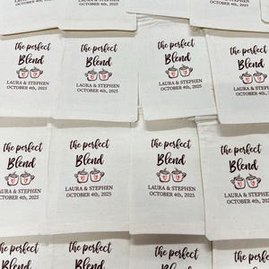 May include: A collection of off-white fabric drawstring pouches featuring the printed text "the perfect Blend" above an illustration of two coffee mugs with red hearts. Below, the text reads "LAURA & STEPHEN OCTOBER 4th, 2025".